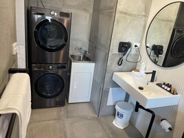 Um banheiro compacto com máquina de lavar, armário pequeno, pia com amenities e espelho.