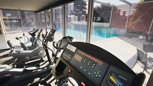A gym with cardio machines and a control panel, overlooking a swimming pool. - Honeysuckle Executive Apartments (Newcastle)