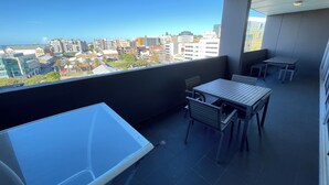 A balcony with a table and chairs, overlooking a cityscape with various buildings. - Honeysuckle Executive Apartments (Newcastle)