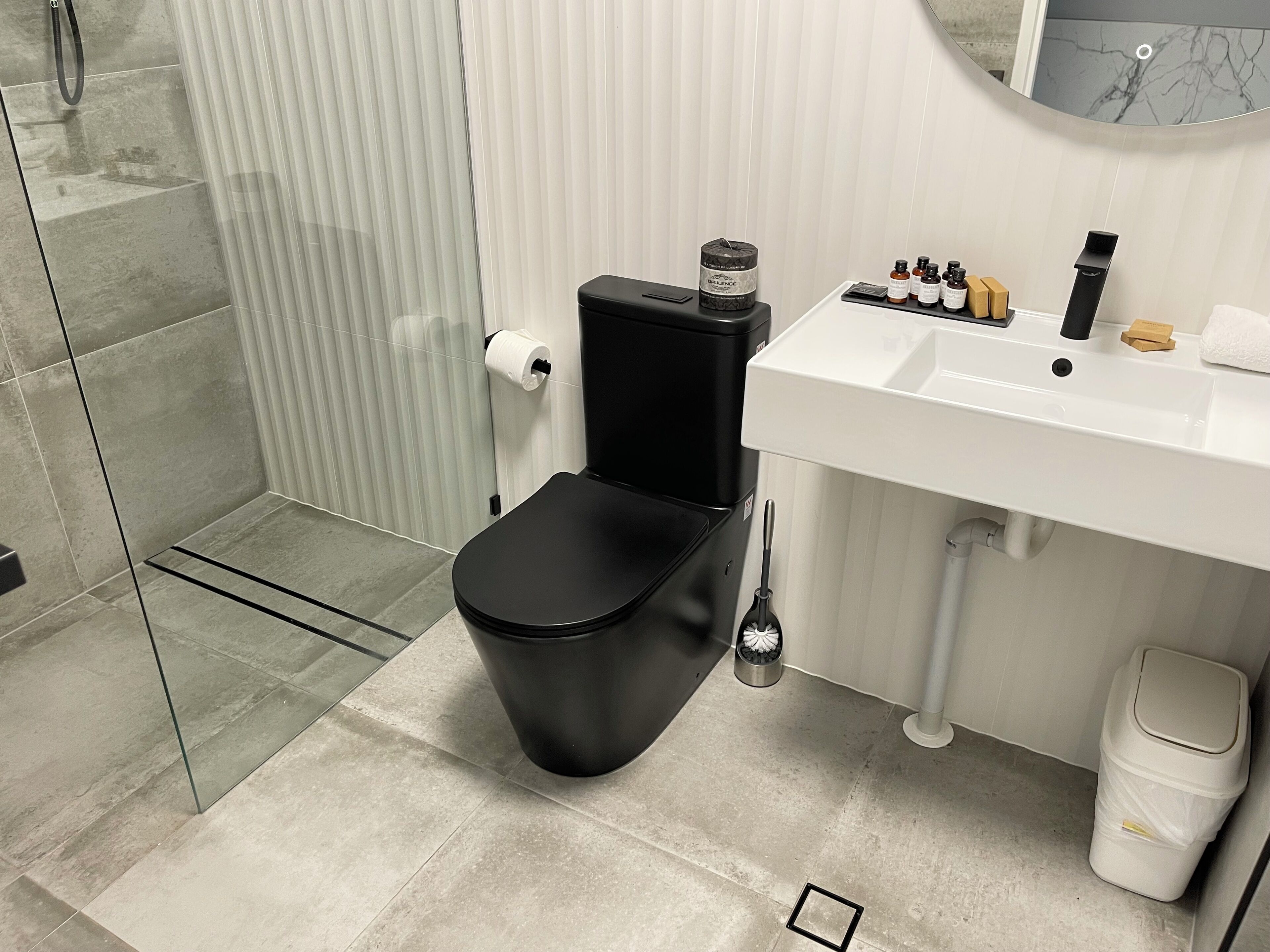 A modern bathroom with a black toilet, white sink, and a glass shower enclosure.