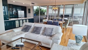 A modern living room with a white sofa, a glass coffee table, and a dining area with a table and chairs. - Honeysuckle Executive Apartments (Newcastle)