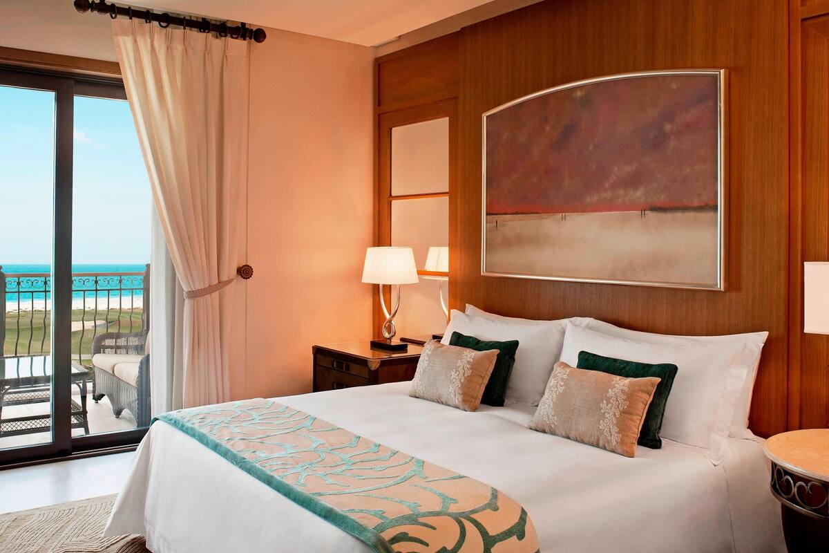 A hotel room with a large bed, a view of the beach, and a painting on the wall.