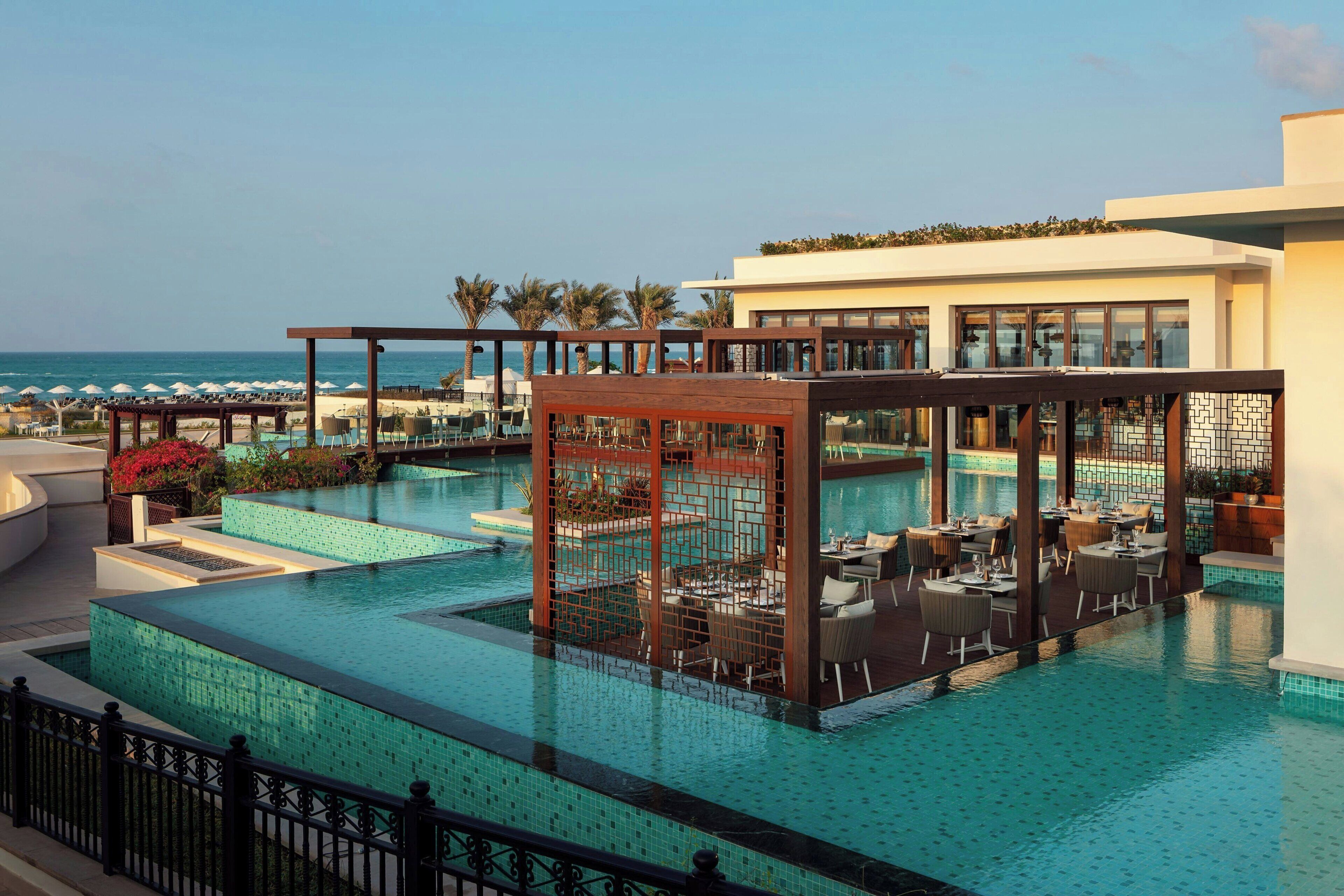 A pool area with multiple seating areas and a view of the ocean.