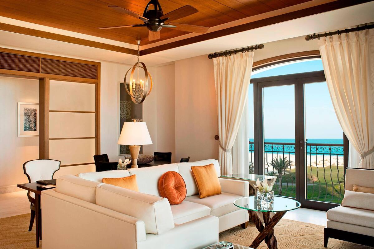 A modern living room with a white sofa, a glass coffee table, and a view of the ocean through large windows.