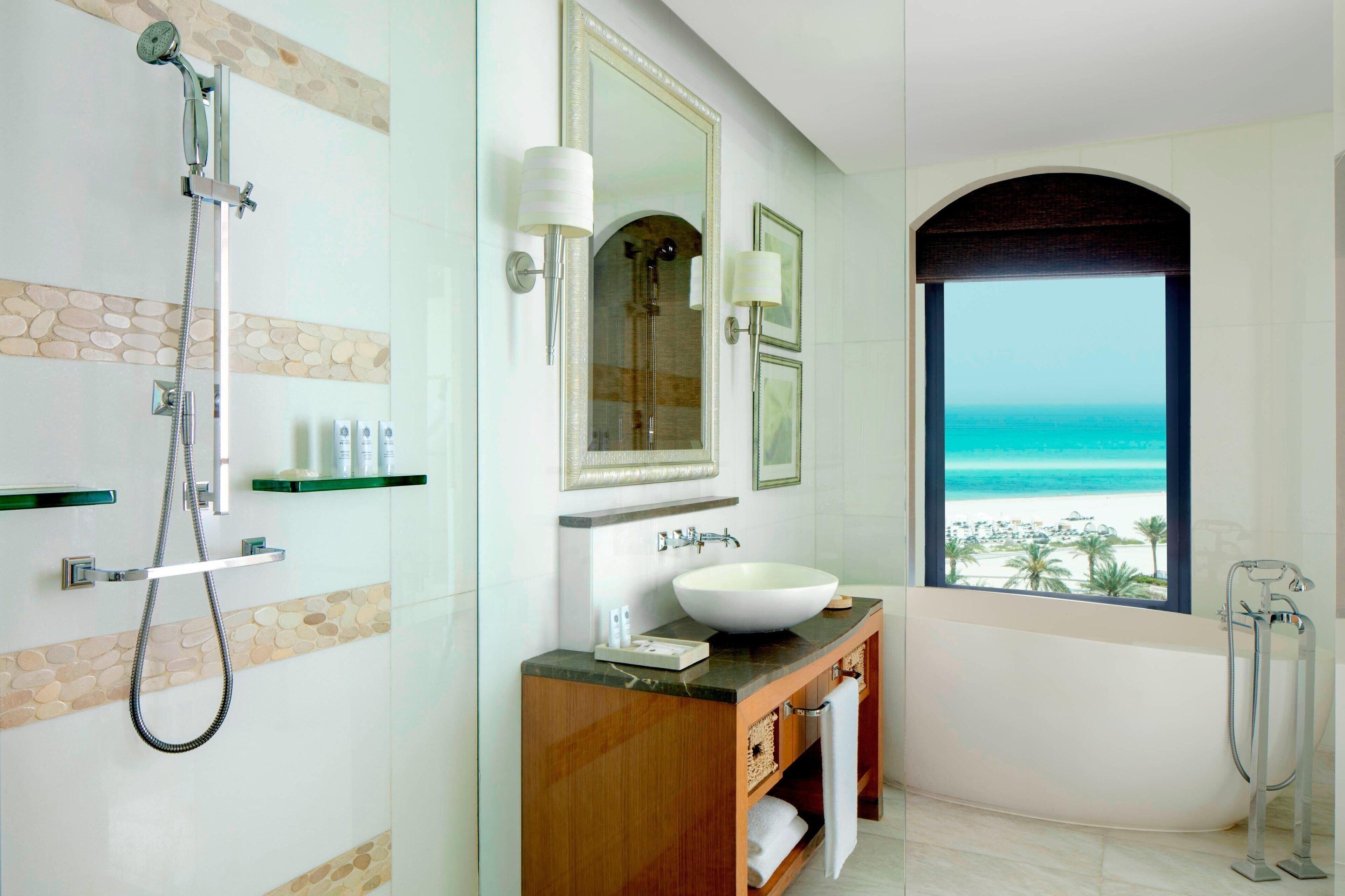 A modern bathroom with a large bathtub, a shower, and a vanity with a sink and mirror. There is a window with a view of the ocean.