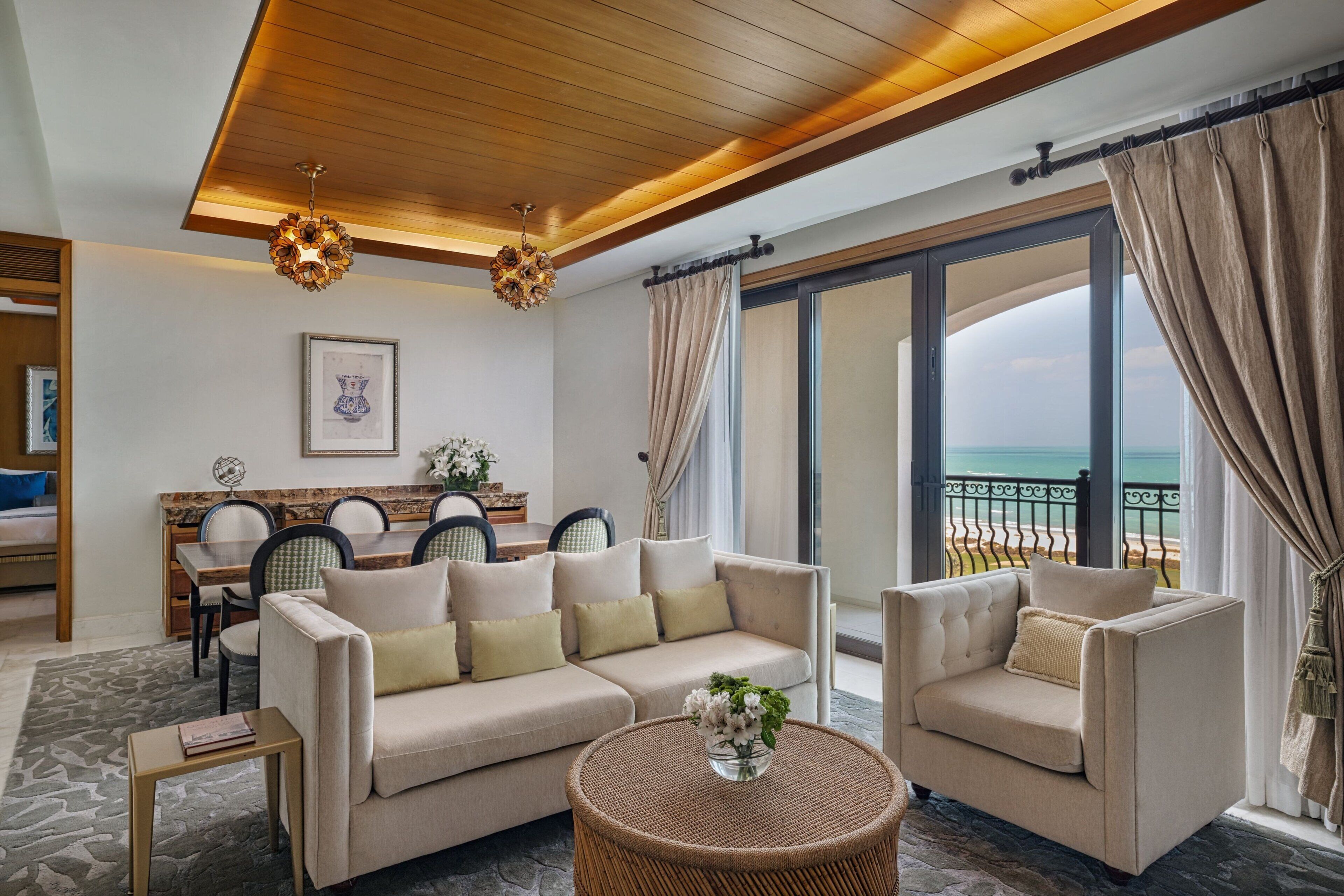 A modern living room with a sofa, armchairs, a dining table, and a view of the sea.