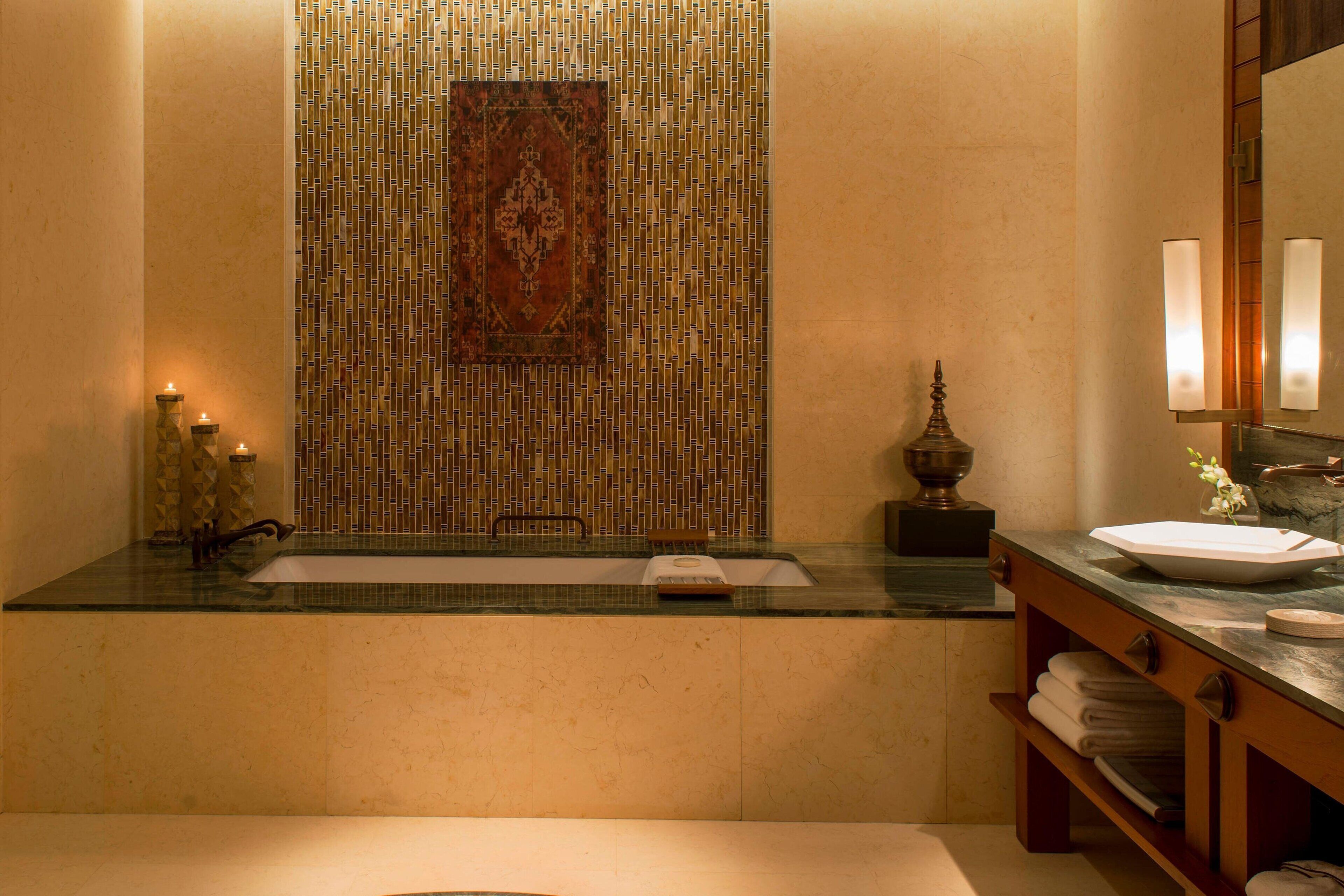 A bathroom with a glass sink, a mirror, a towel rack, and a decorative rug.