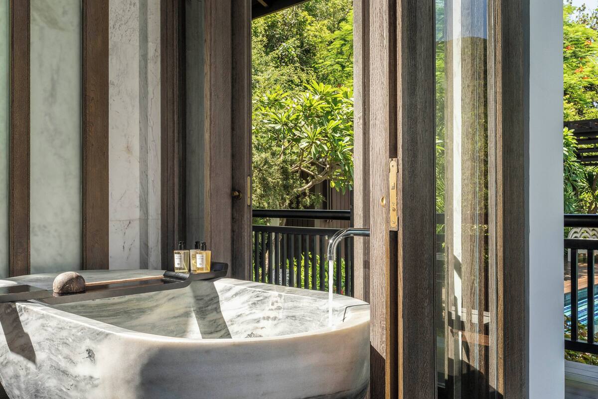 A spa area with a large marble bathtub, wooden columns, and a view of lush greenery.