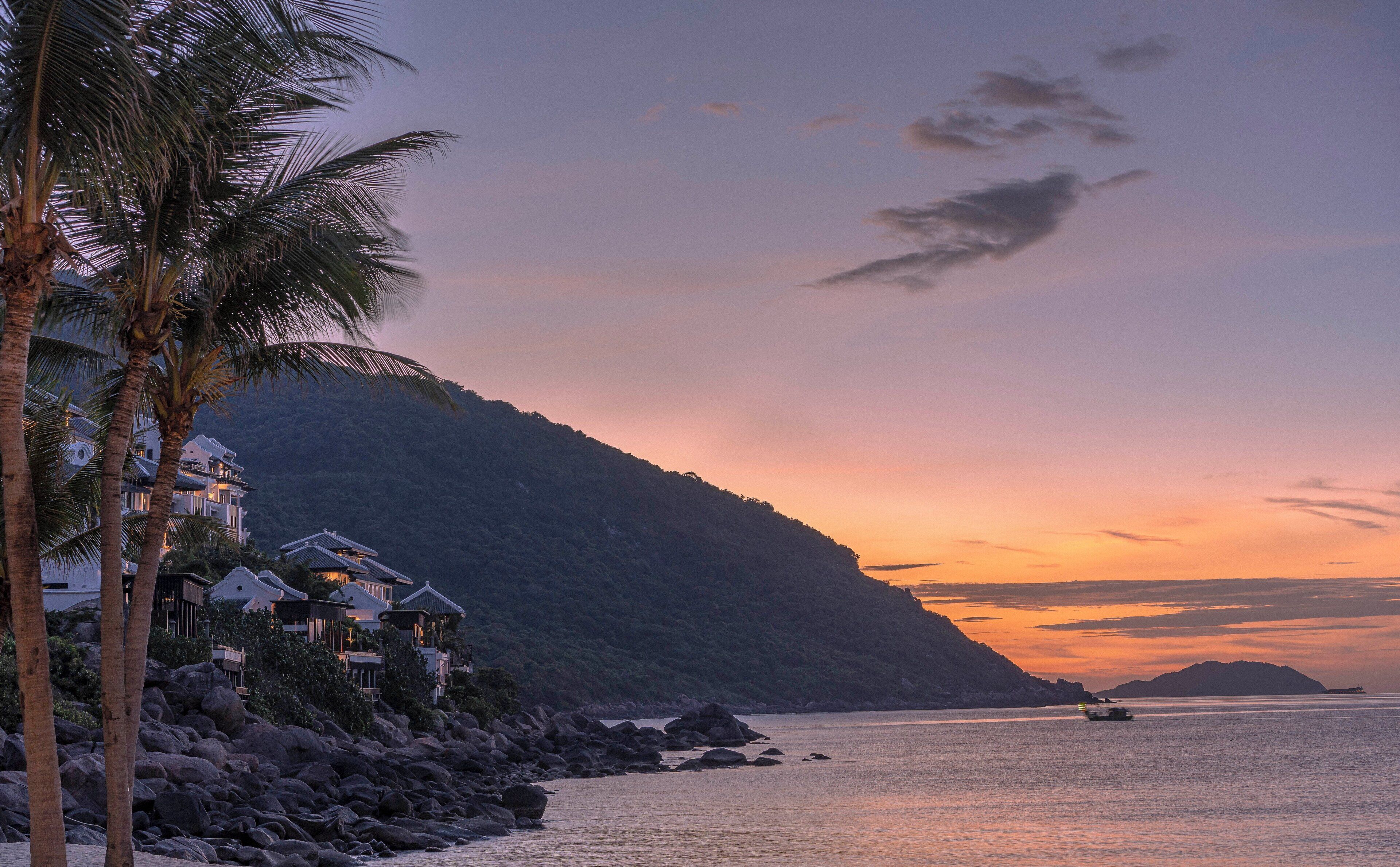 A coastal property with multiple buildings, a rocky shoreline, and a sunset over the water.