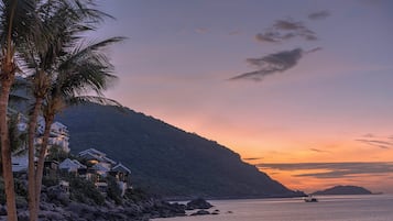 A coastal property with multiple buildings, a rocky shoreline, and a sunset over the water.