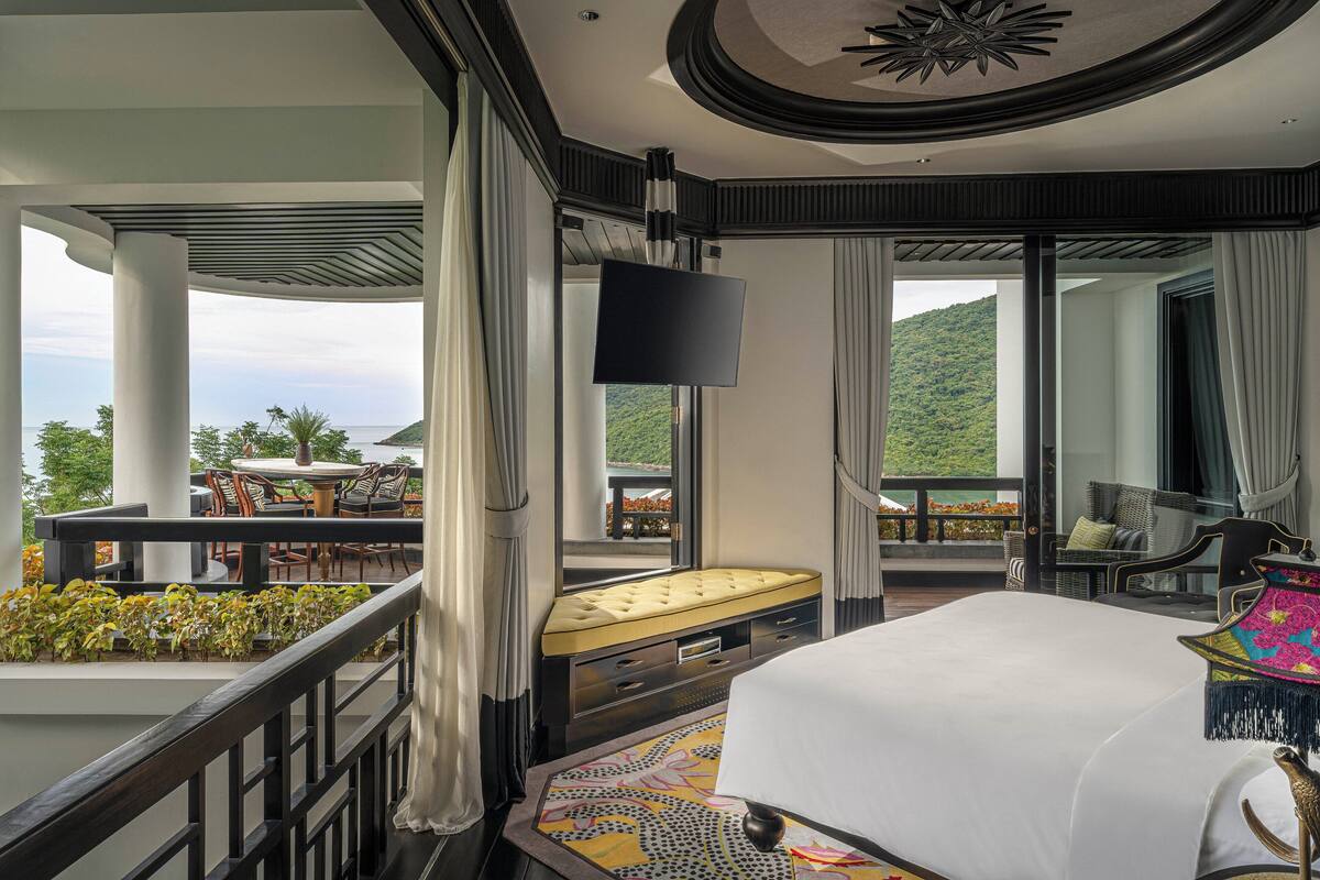A hotel room with a balcony, a bed, a TV, and a dining area with outdoor seating.