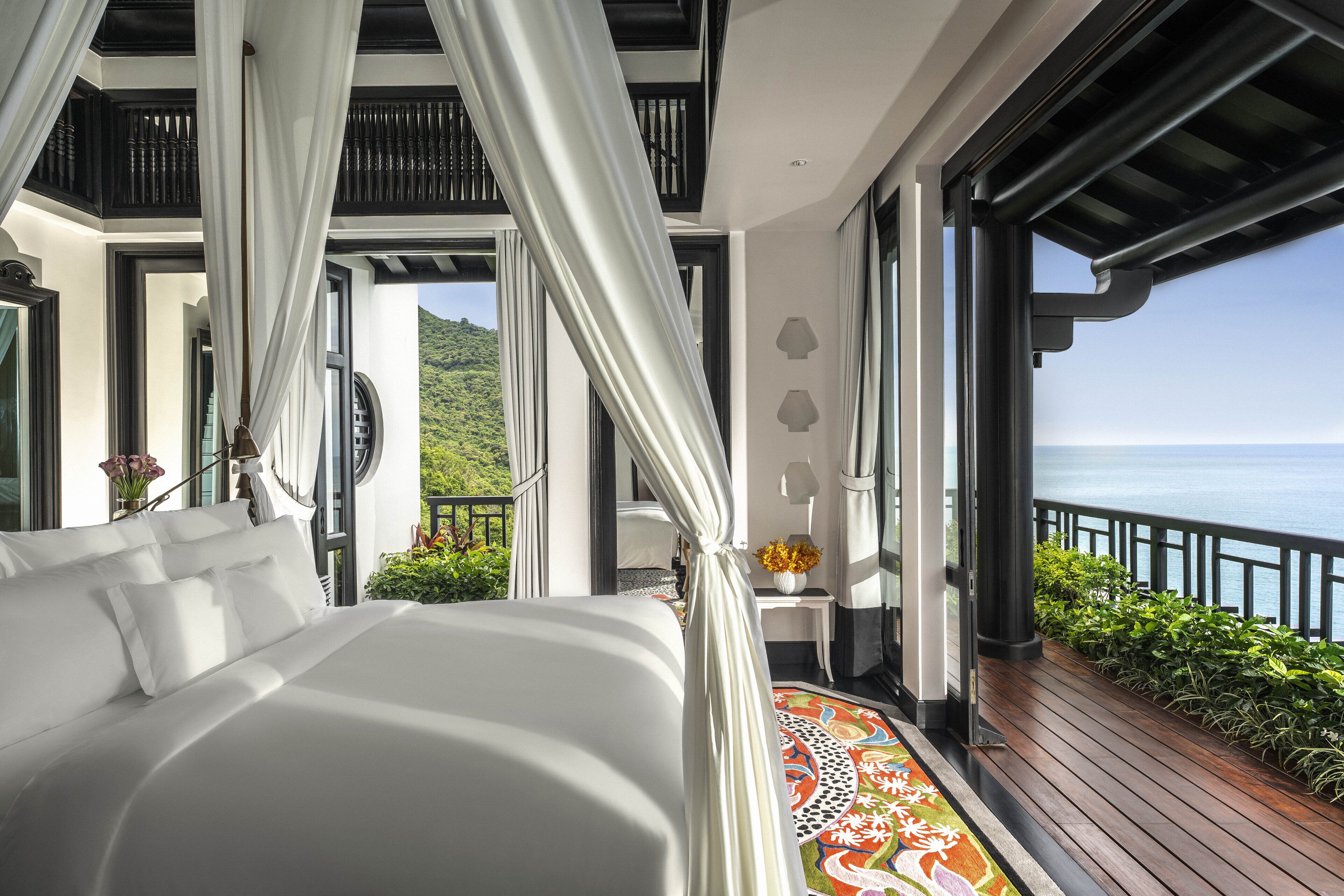 Une chambre avec un grand lit, un balcon donnant sur la mer et un paysage tropical en arrière-plan.