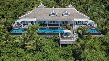 A large house with multiple swimming pools surrounded by lush greenery.