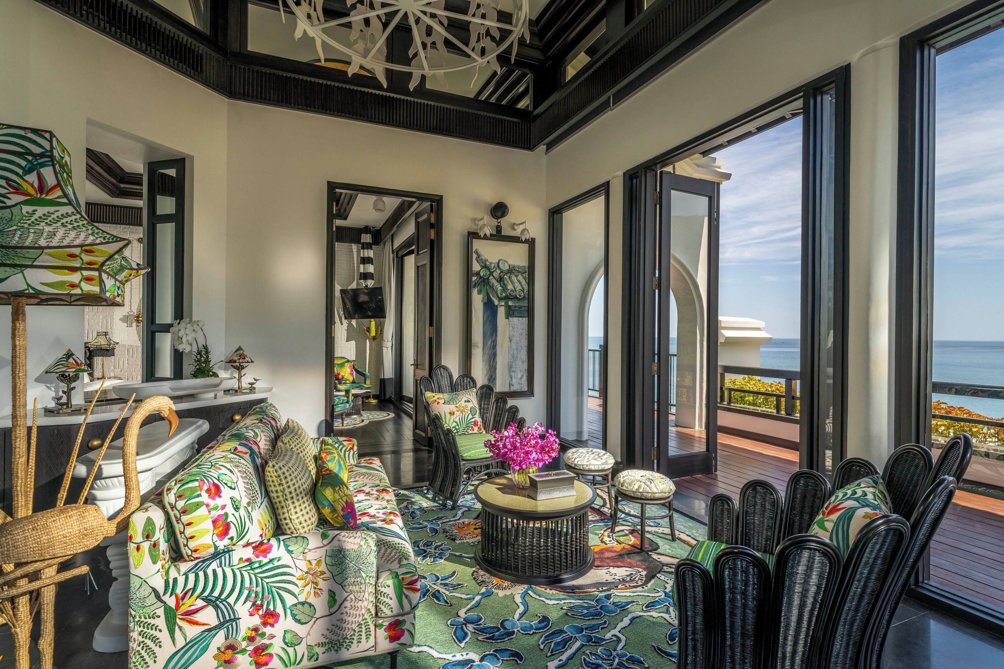 A spacious living area with a large window offering a view of the sea, a colorful patterned sofa, and a variety of decorative items.