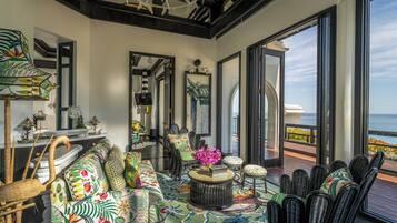 A spacious living area with a large window offering a view of the sea, a colorful patterned sofa, and a variety of decorative items.