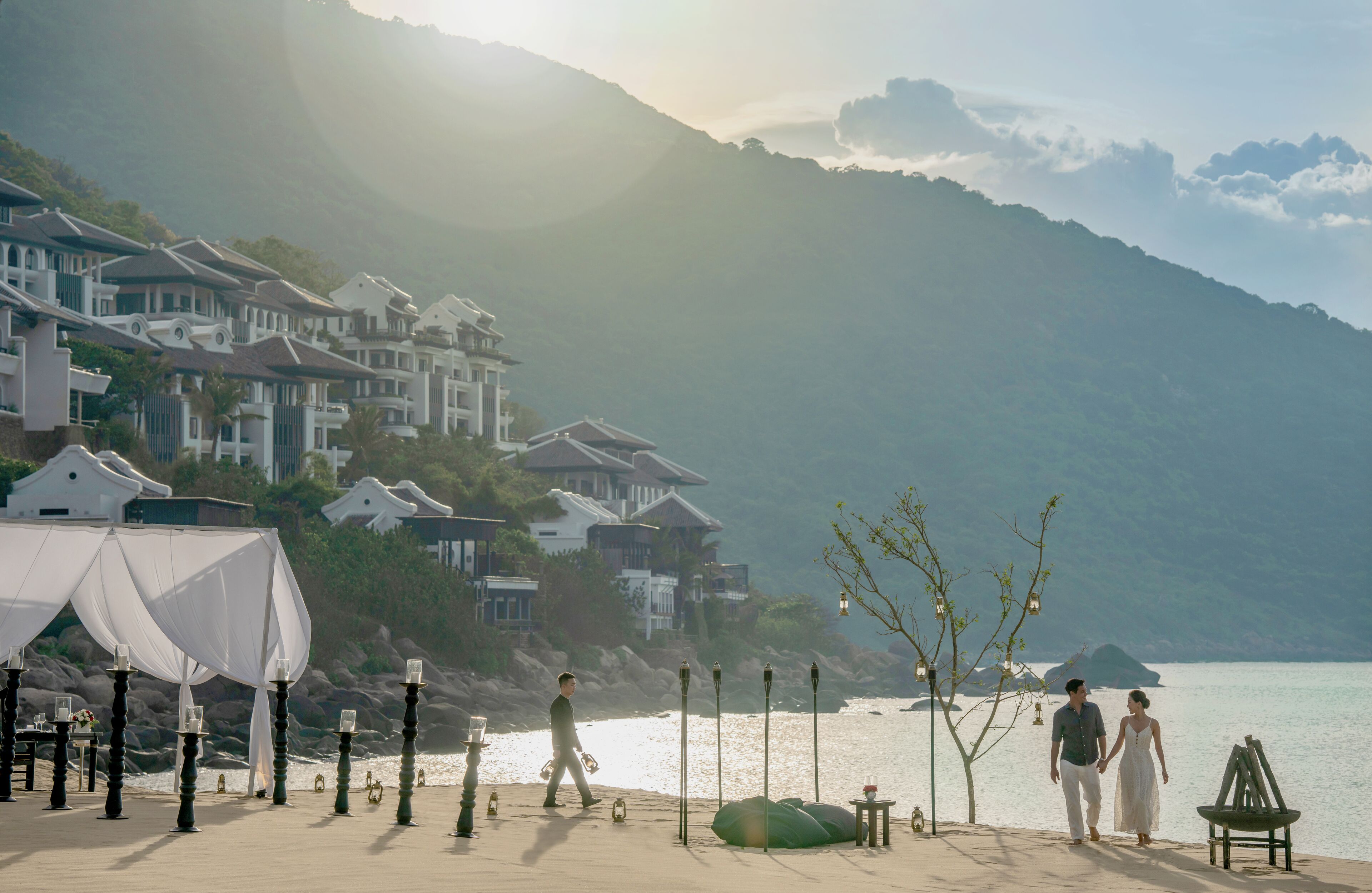 A coastal area with a beach, a row of houses, and a couple walking.