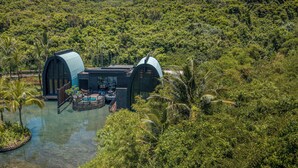 Una villa moderna con due ampie strutture ad arco, una piscina e rigogliosa vegetazione tutt'intorno.