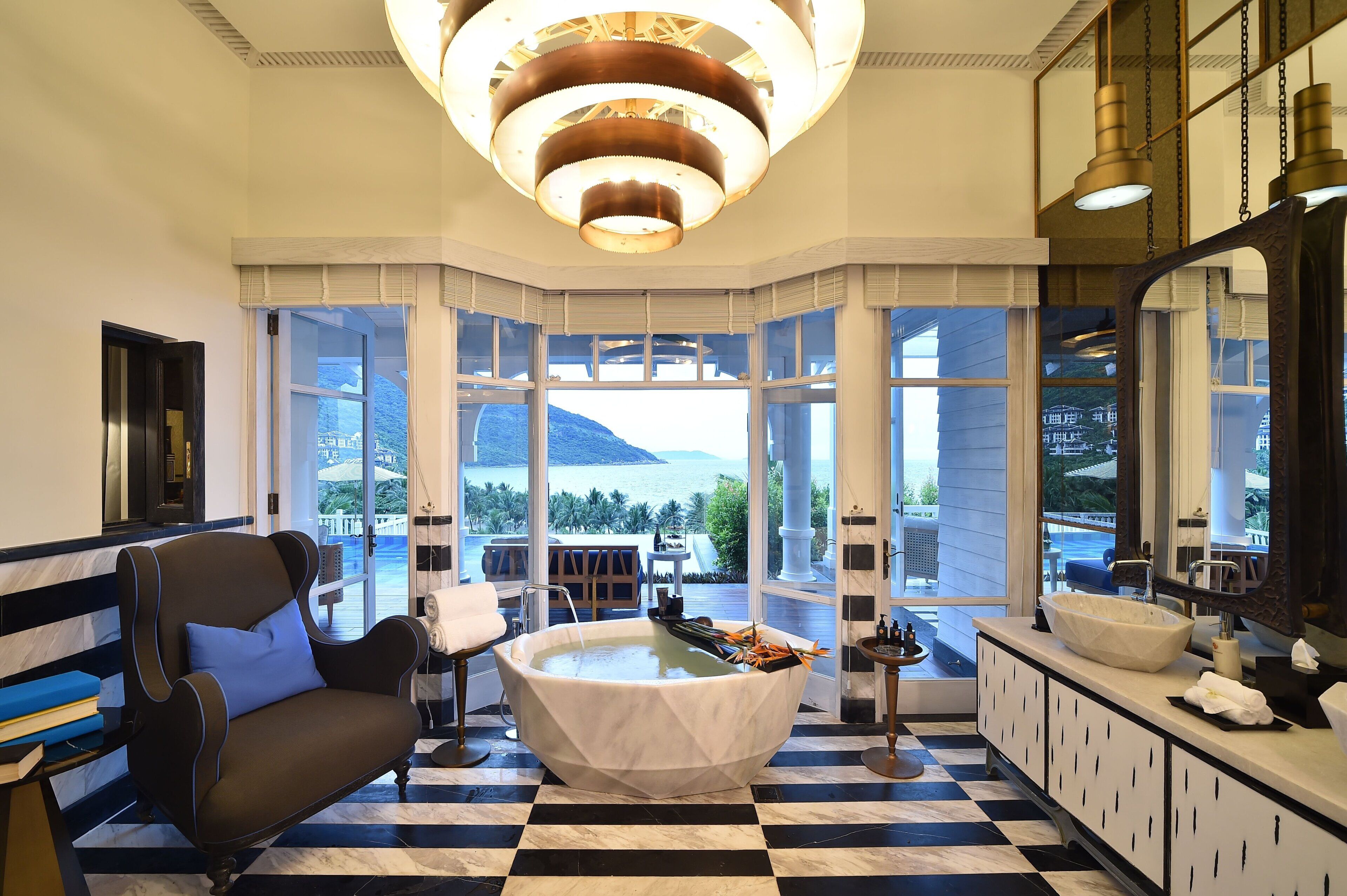 A luxurious bathroom with a large bathtub, a seating area with a chair and a table, and a view of the sea through large windows.