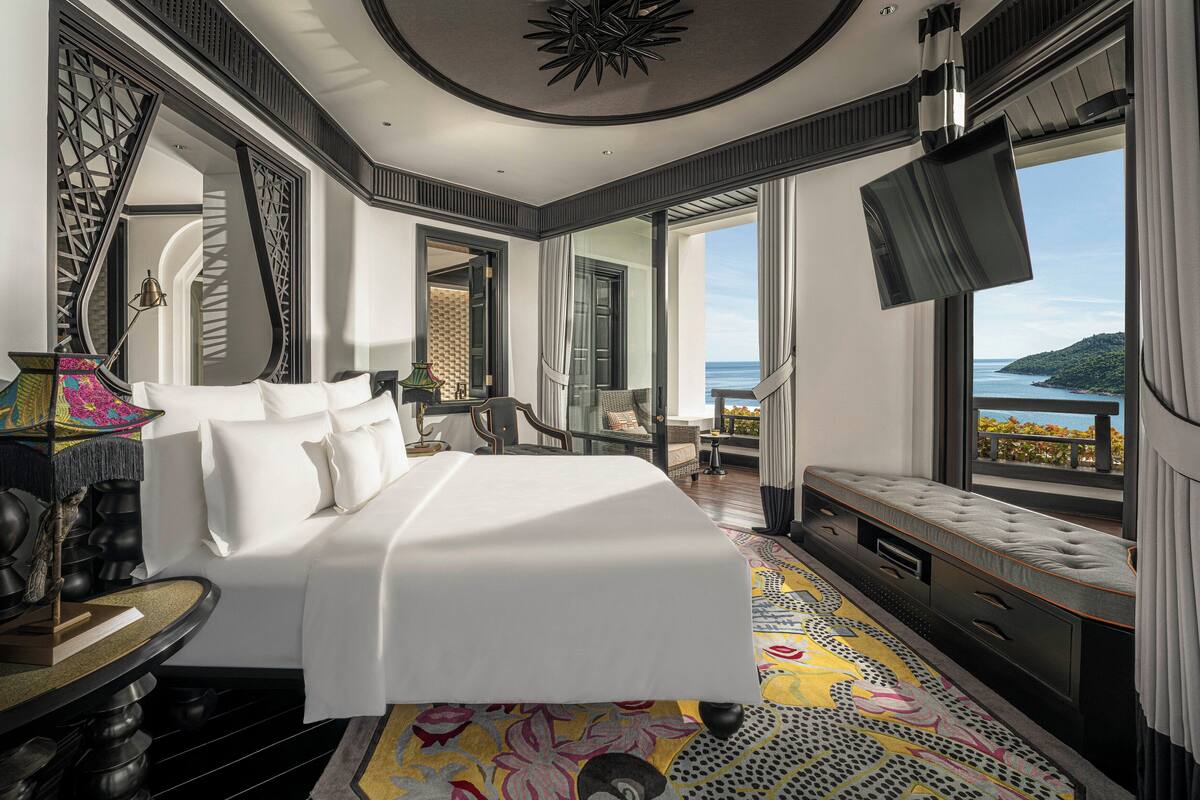 A spacious bedroom with a large bed, a TV, and a balcony with a view of the sea.