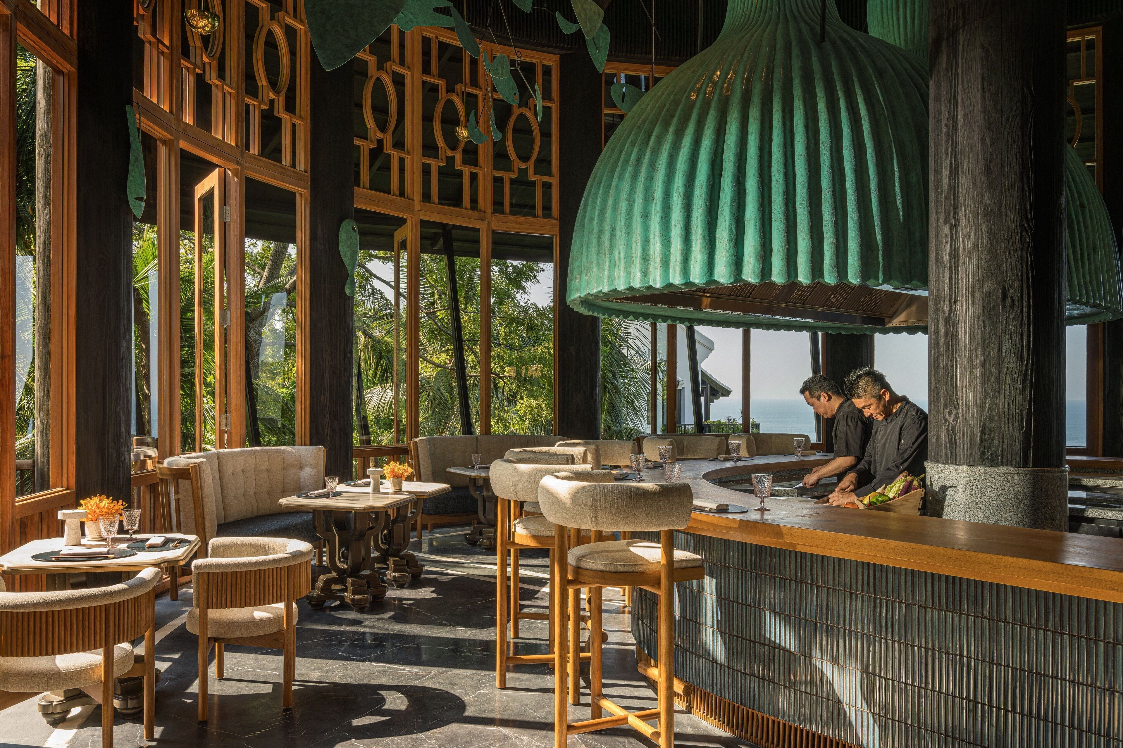 Ein Restaurant mit Holztischen, einer Bar und großen Fenstern mit Blick ins Freie.