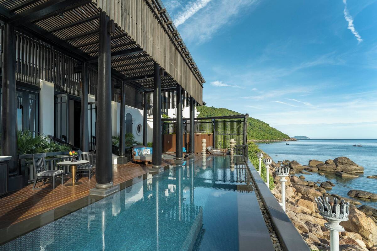 An infinity pool with a wooden deck, outdoor seating, and a view of the sea.