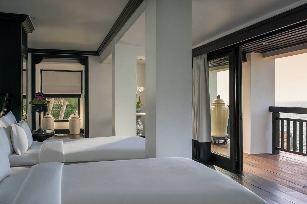 A hotel room with two beds, a balcony with a view, and a large window with curtains.