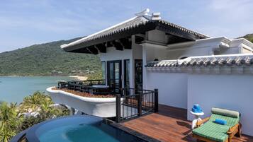 A modern villa with a private pool, a balcony with a view of the sea, and a lounge area with a chair and a table.