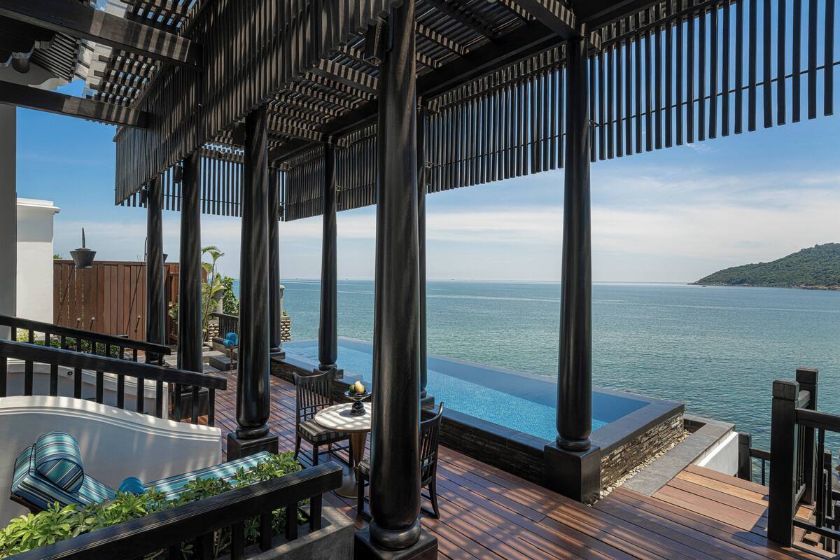 A wooden deck with a pool, columns, and a view of the sea.