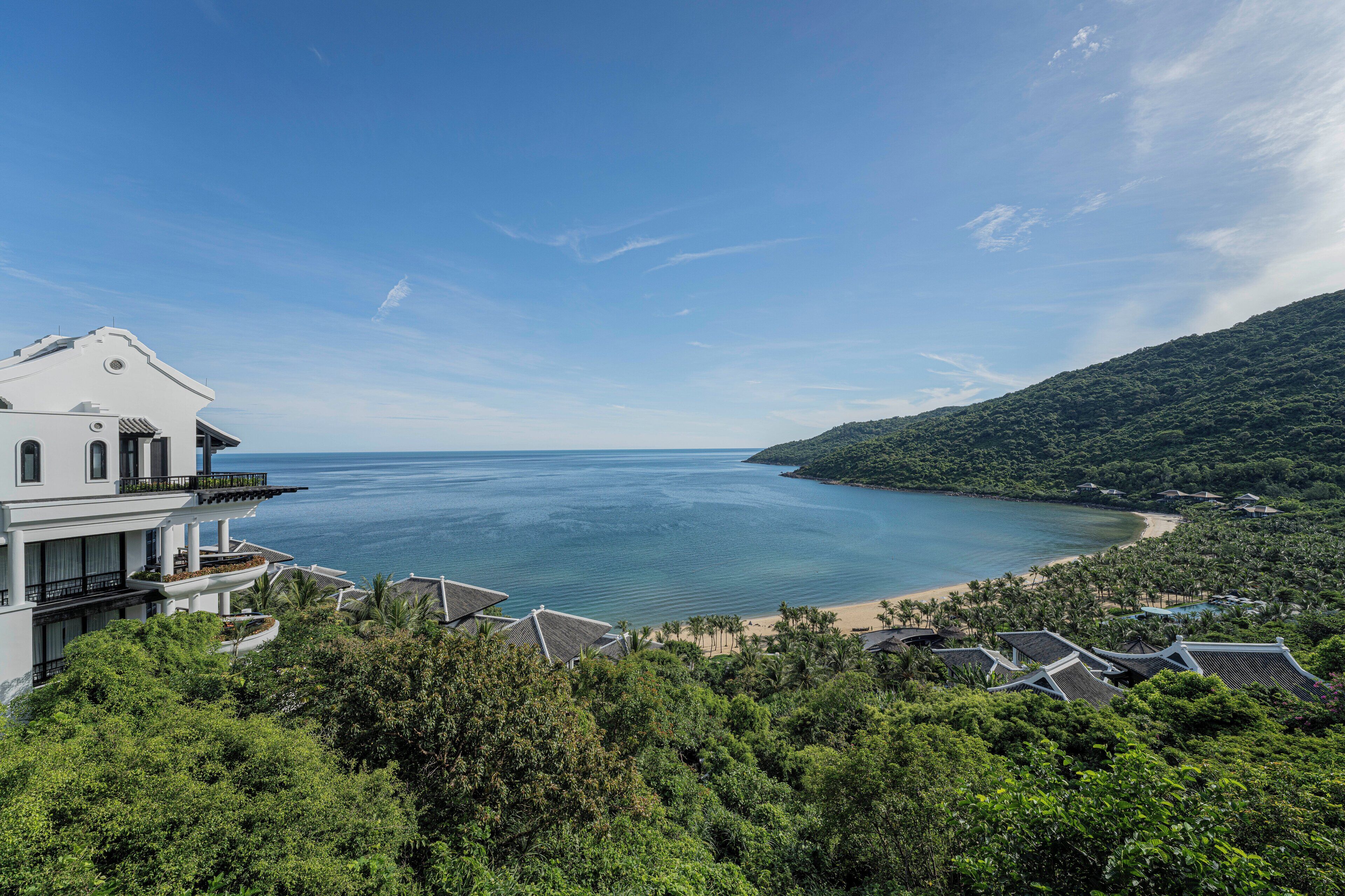 A coastal property with a large white building, a beach, and lush greenery.