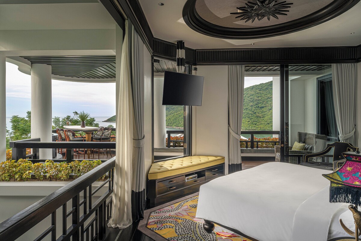 A hotel room with a balcony, a bed, a TV, and a dining area with outdoor seating.