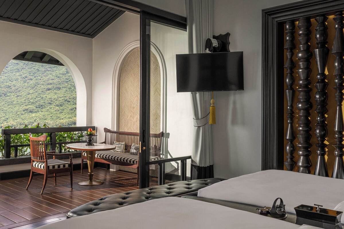 A hotel room with a balcony, a bed, a TV, and a view of the forest.