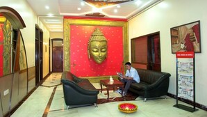 A lobby with a Buddha statue, a sofa, a coffee table, a newspaper stand, and a decorative lamp. - Hotel Sita International (New Delhi)
