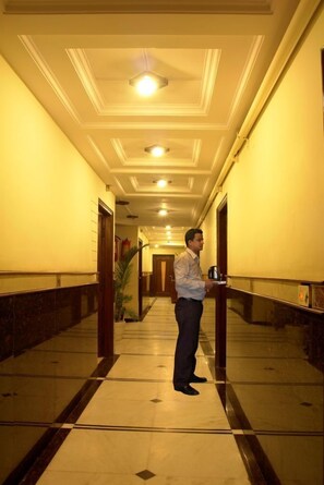 A hotel corridor with a marble floor, a person holding a tray, and a ceiling with recessed lighting. - Hotel Sita International (New Delhi)