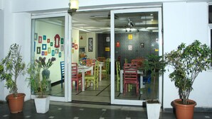 A restaurant with a glass door entrance, indoor plants, and a tiled floor. - Hotel Sita International (New Delhi)