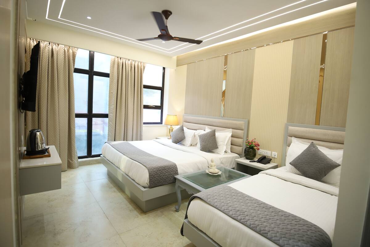 Habitación de hotel con dos camas, ventilador de techo, mesita de noche con lámpara y ventana con cortinas.