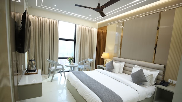 A modern hotel room with a large bed, a ceiling fan, a desk with a lamp, and a view of the outdoors. - Hotel Sita International (New Delhi)