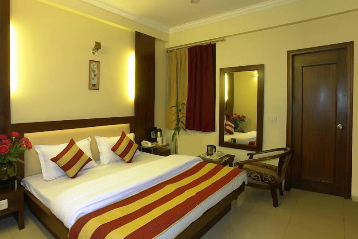 Una habitación de hotel con una cama, una mesita de noche, una silla, un espejo y una puerta.