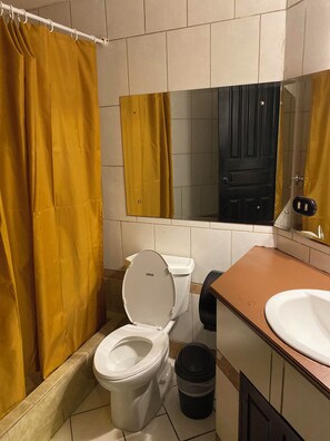 Een badkamer met toilet, wastafel, prullenbak en douchegordijn.