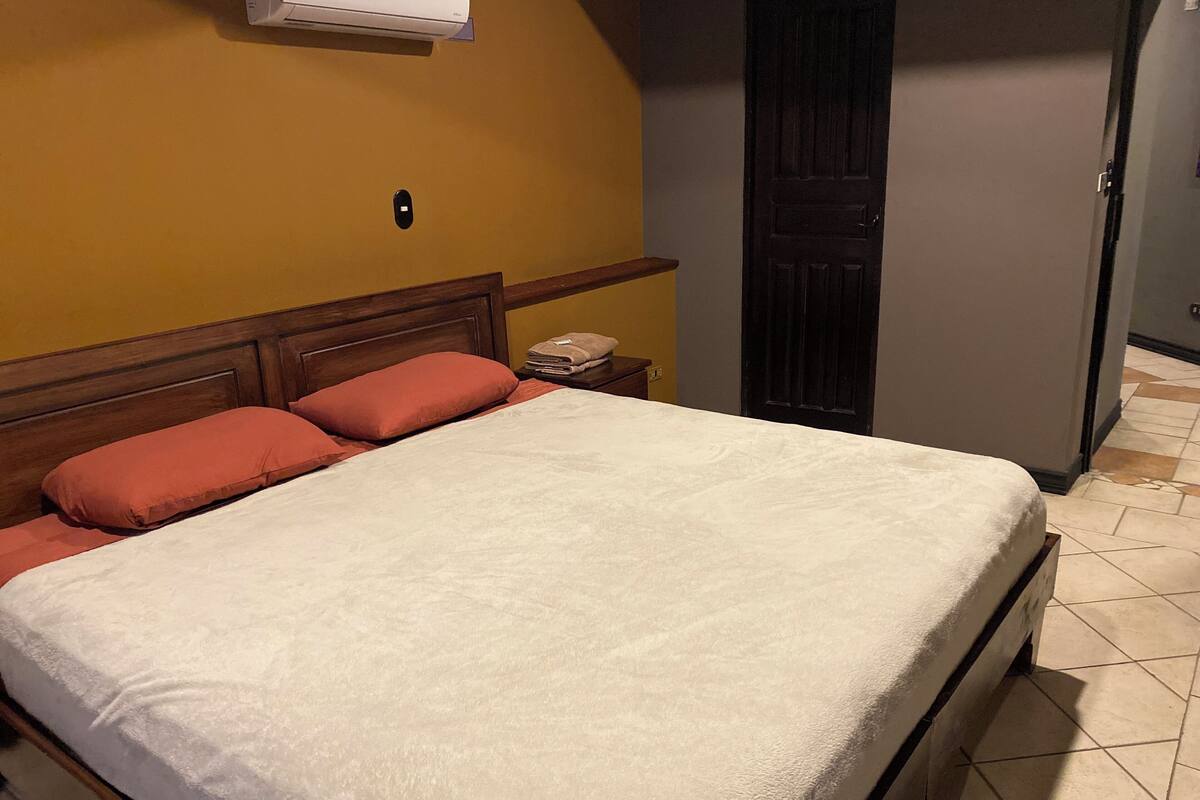 Quarto com cama, mesa de cabeceira, ar-condicionado fixado na parede e porta.