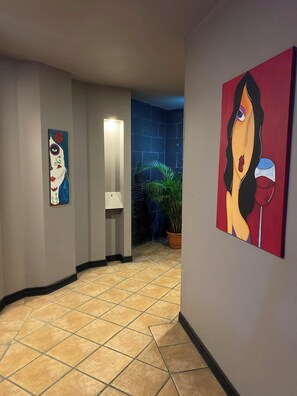 Een gang met betegelde vloer, een kamerplant en twee kunstwerken aan de muur.