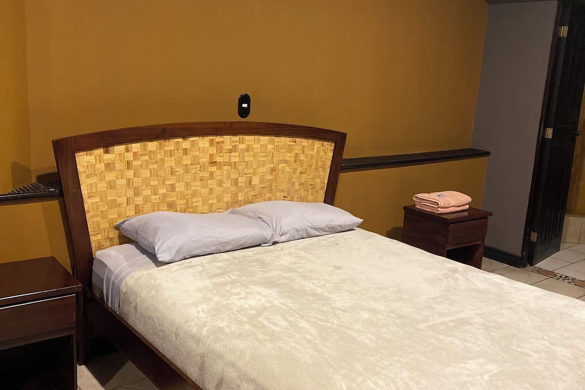 Quarto de hotel com cama, cabeceira de madeira e ar condicionado fixado na parede.