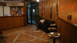 Zona de recepció amb taulell de recepció, un rellotge, una planta i una zona d'estar amb tamborets.