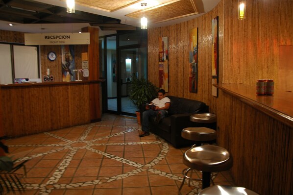 A reception area with a reception desk, a clock, a plant, and a seating area with stools.