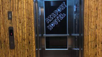 Un ascensor con un cartel que dice "Airport Hostel" y una pared de bambú.