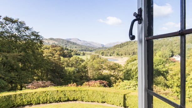 Vista a través de una ventana de un paisaje exuberante con colinas ondulantes y un río.