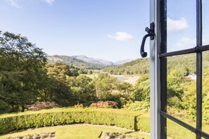 A view through a window of a lush landscape with rolling hills and a river. - Nanny Brow (Ambleside)