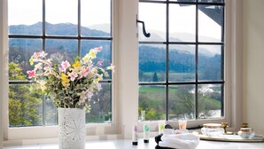 Una ventana con vistas a montañas, un florero con flores y artículos de tocador en el alféizar.