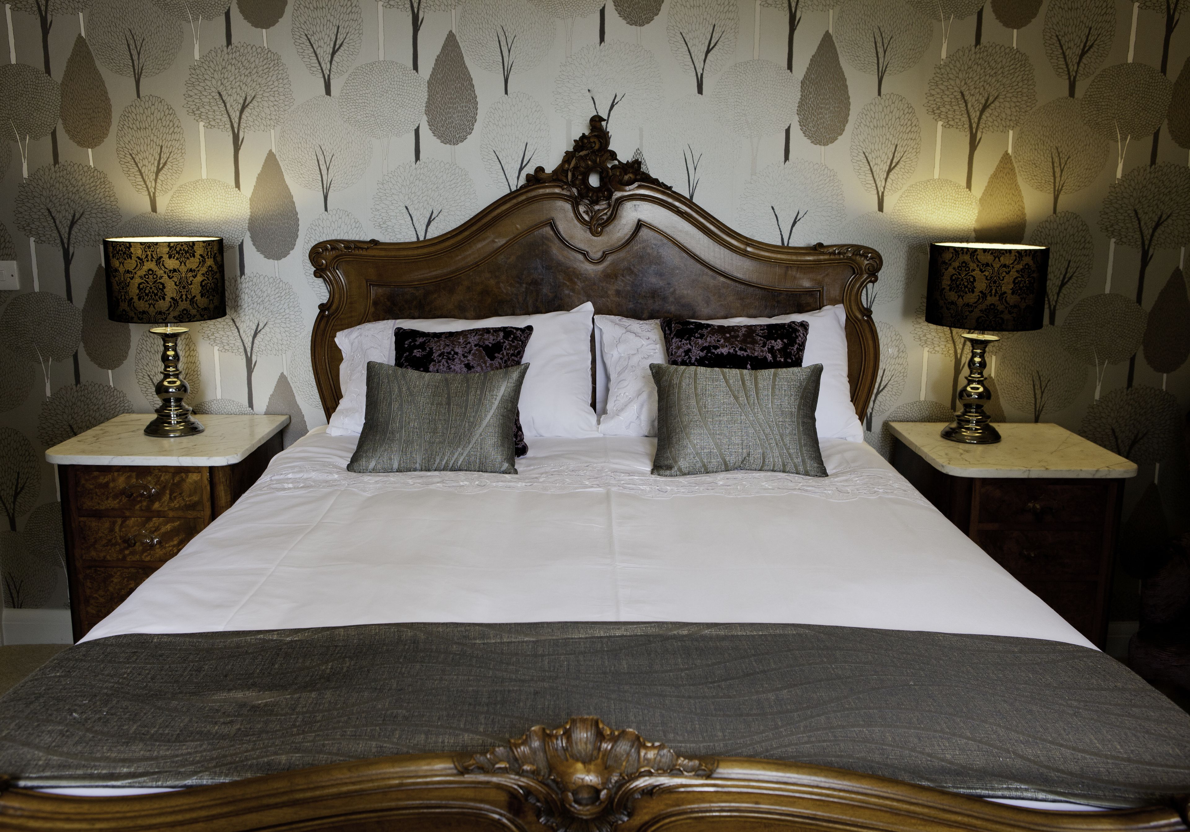 A neatly made bed with a wooden headboard, two bedside tables with lamps, and a patterned wallpaper.