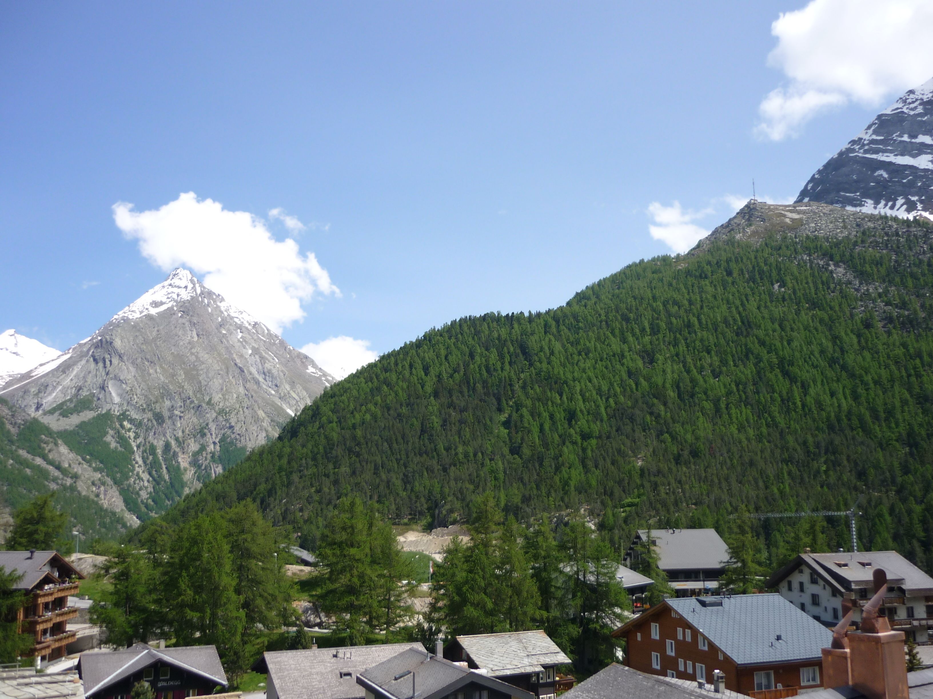A mountain village with traditional wooden houses, a ski lift, and a prominent snow-capped peak in the background.