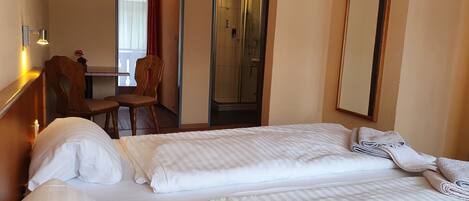 A hotel room with a bed, a desk, a chair, and a shower area.